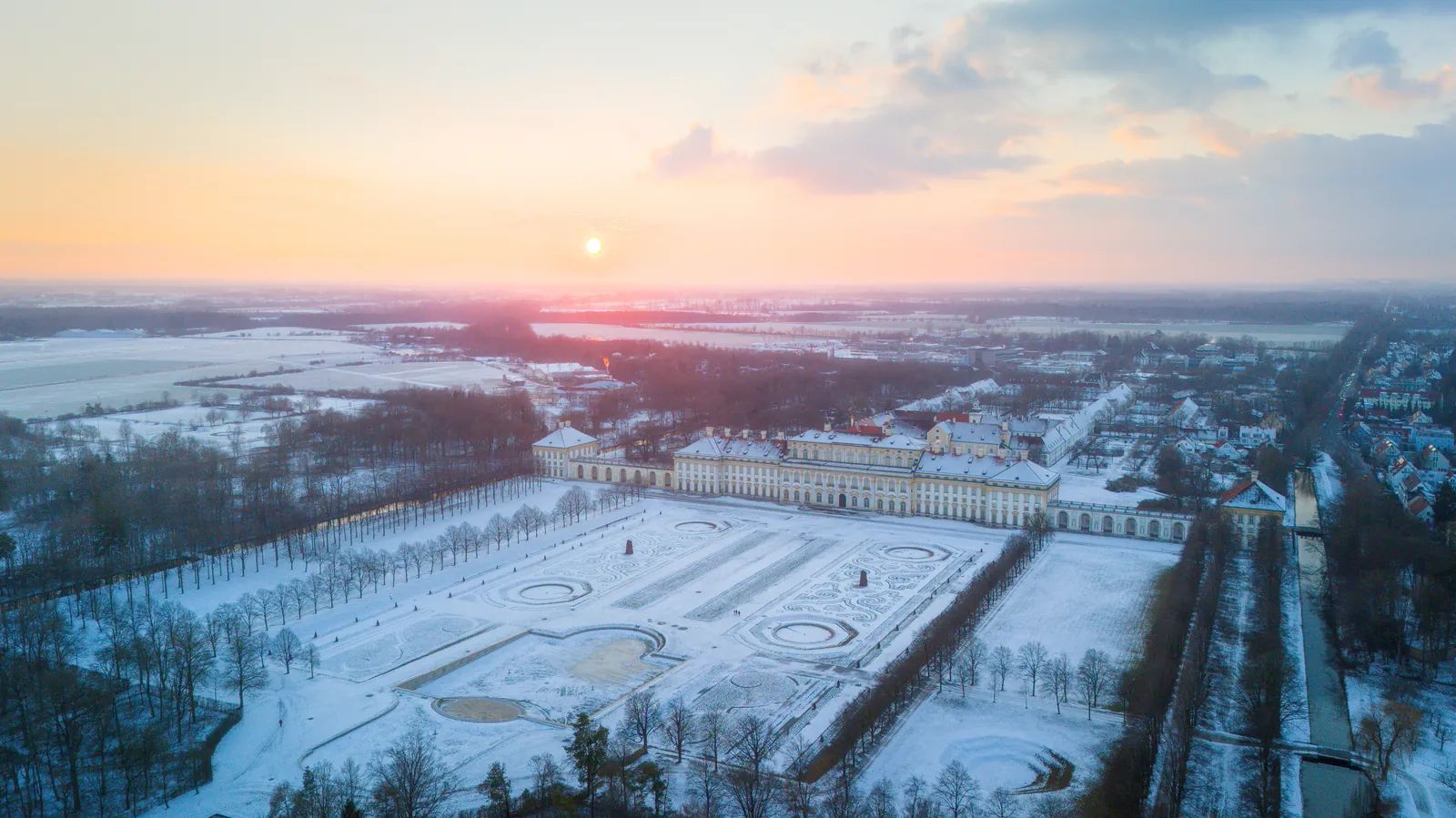 Luftbild einer verschneiten Schlossanlage bei Sonnenuntergang