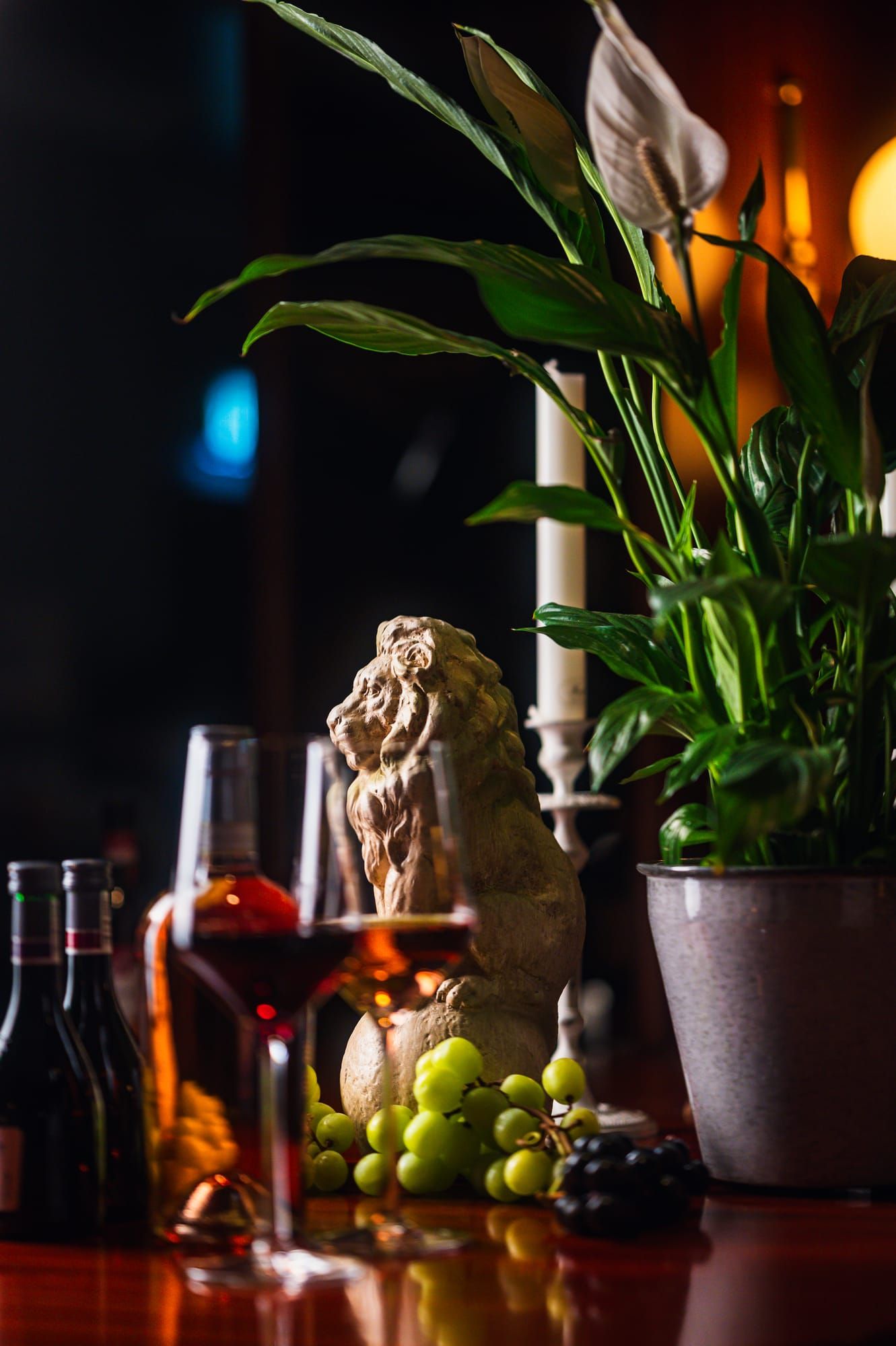 Rotwein, Trauben und eine Löwenfigur vor dunklem Hintergrund